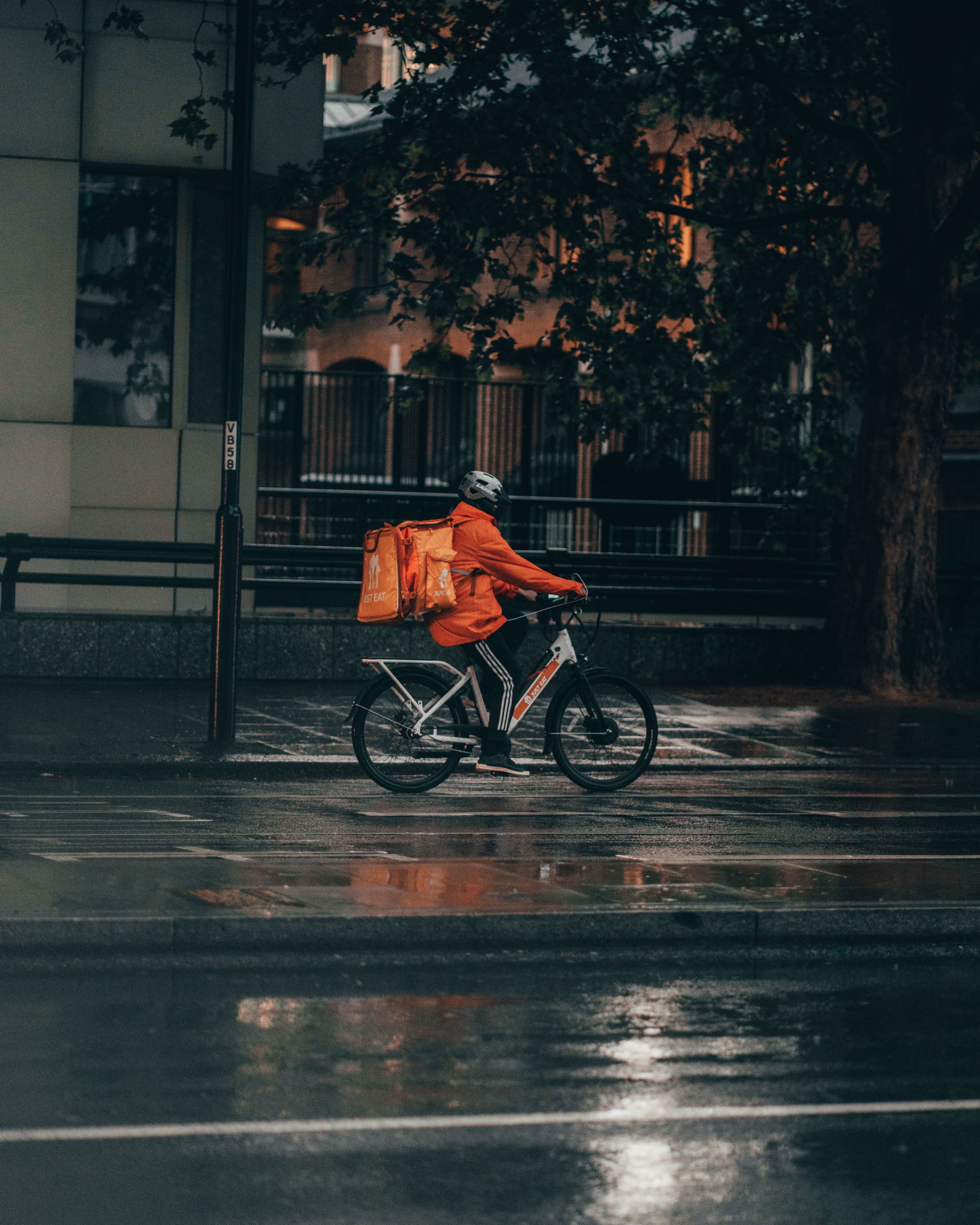 Delivery worker riding a bike at night in the rain.